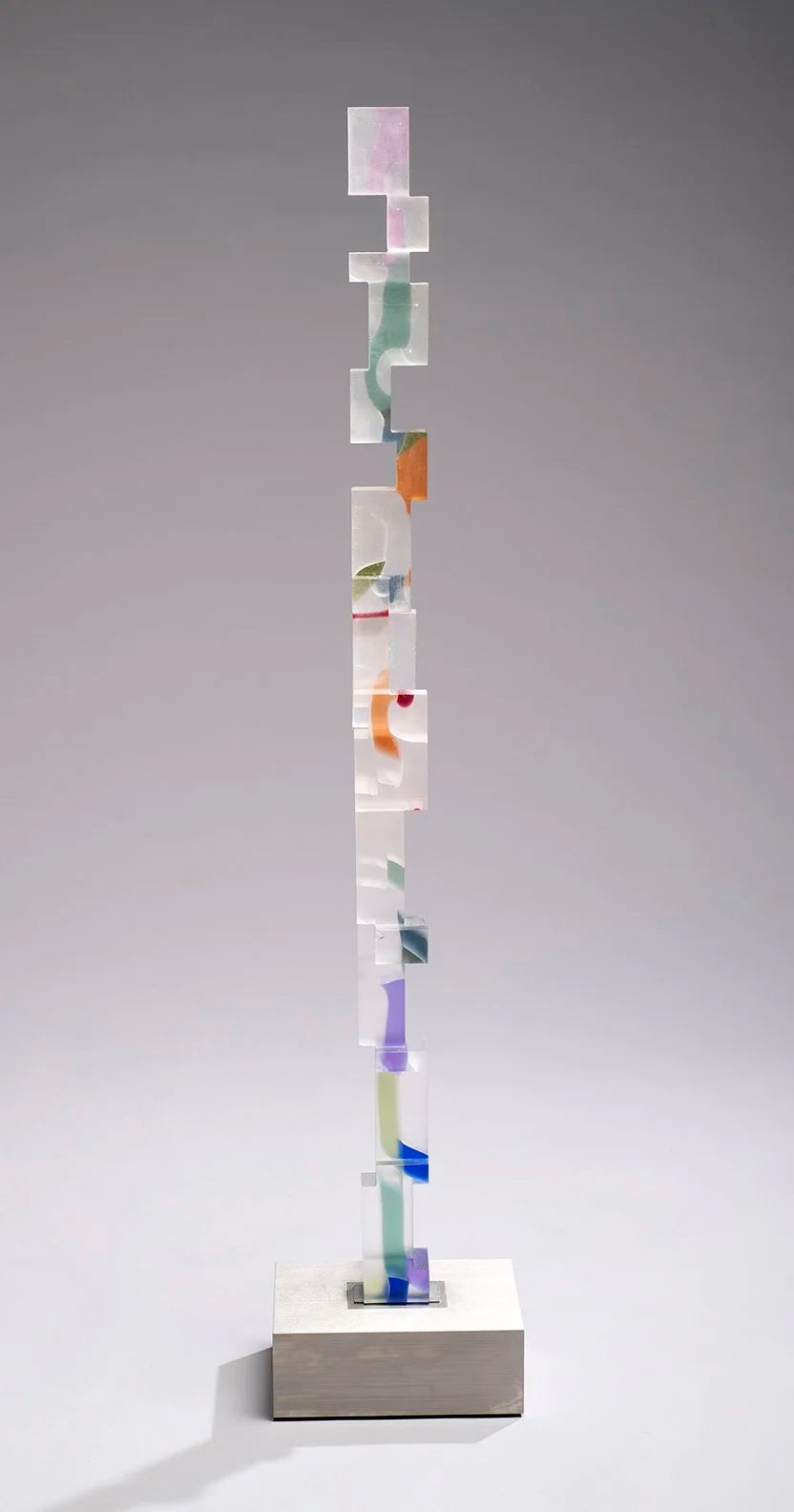 Frosted glass column of notched, interlocking blocks with suspended flecks of orange, violet, blue and sage on a steel base.