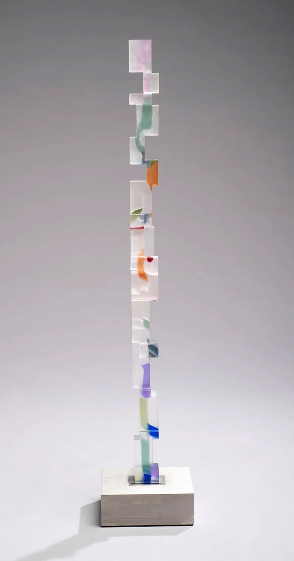 Frosted glass column of notched, interlocking blocks with suspended flecks of orange, violet, blue and sage on a steel base.