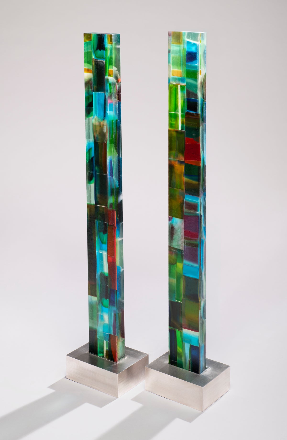 Tall glass column made of mosaic-like panels in emerald, teal, cobalt and crimson on a brushed stainless steel base.
